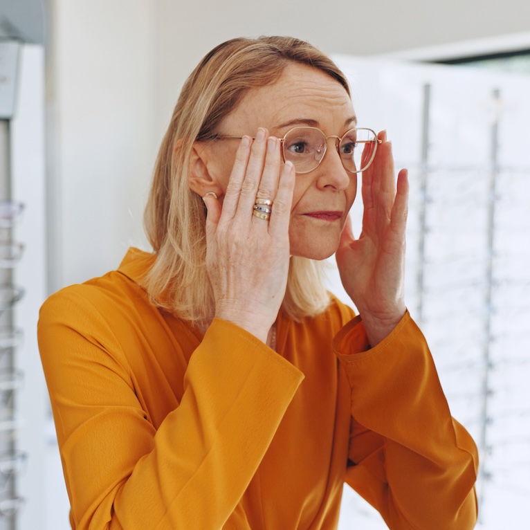 Woman, glasses and shopping with check, mirror or clinic for healthy vision with optometry service for wellness. Mature person, client or customer for decision, prescription eyewear or frame at store Eye disease management including glaucoma, cataracts, and macular degeneration